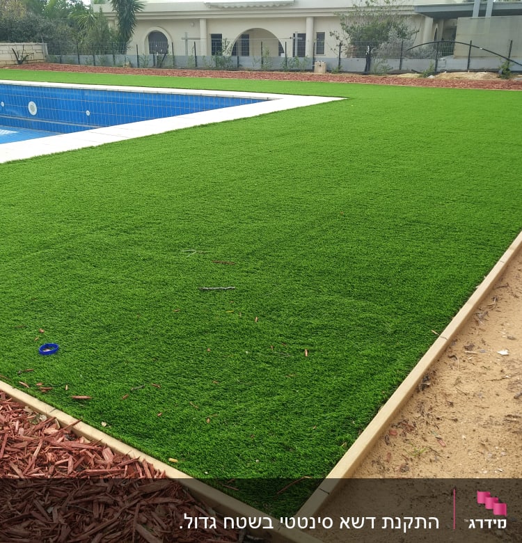 דשא סינתטי ליד בריכה עם שבבי עץ